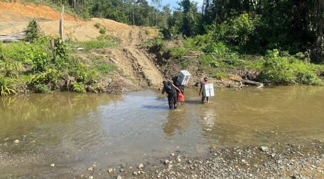 Tampak personil Polres Keerom Briptu Muflihuddin dan Bripda Rian Merahabia ketika menyeberangi sungai ketika melakukan pengawalan logistik Pemilu 2024 menuju Kampung Milki, Distrik Towe, Keerom pada 15 Februari 2024 silam / Istimewa